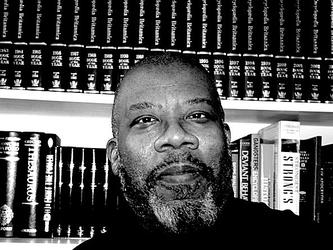 black and white image of Dr Kenny Monrose into front of a book shelf